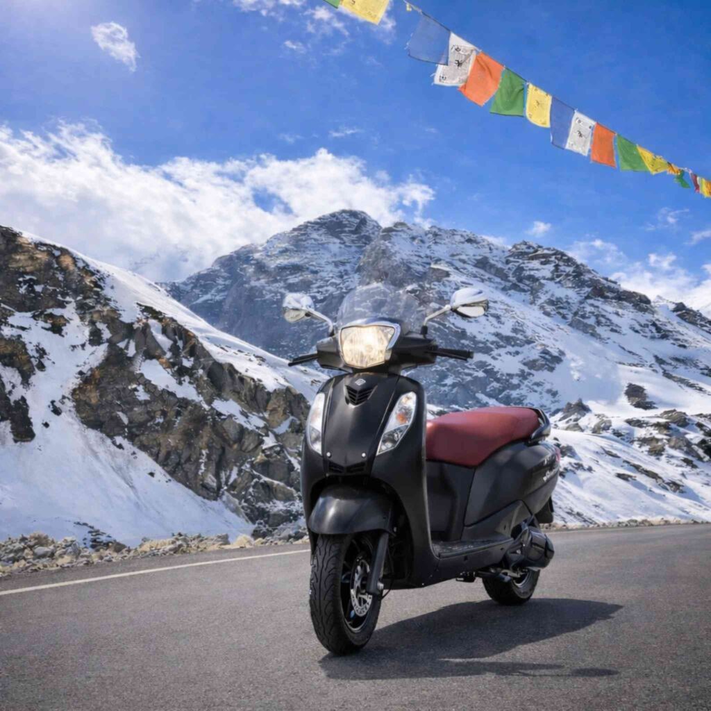 Suzuki Access 125 scooty for rent in Manali on mountain road with snow peaks and prayer flags